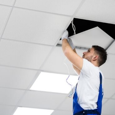 Full Length Portrait Of Electrician On Stepladder Installs Lighting To The Ceiling In Office